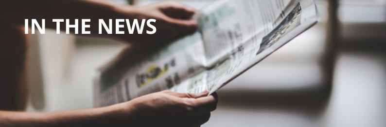 Background of someone holding a newspaper with "IN THE NEWS" written in white, caps letters over top of it