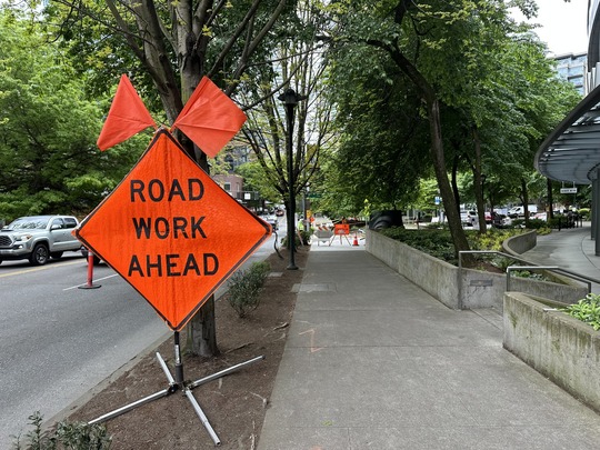 Construction sign reading "Road Work Ahead" with sidewalk detour signs in the background