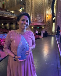 Rita Meher standing on Paramount stage holding mayors film award