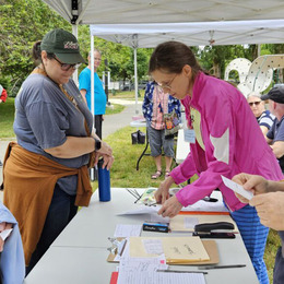 People at a table under a tent giving out information sheets and talking to participants.