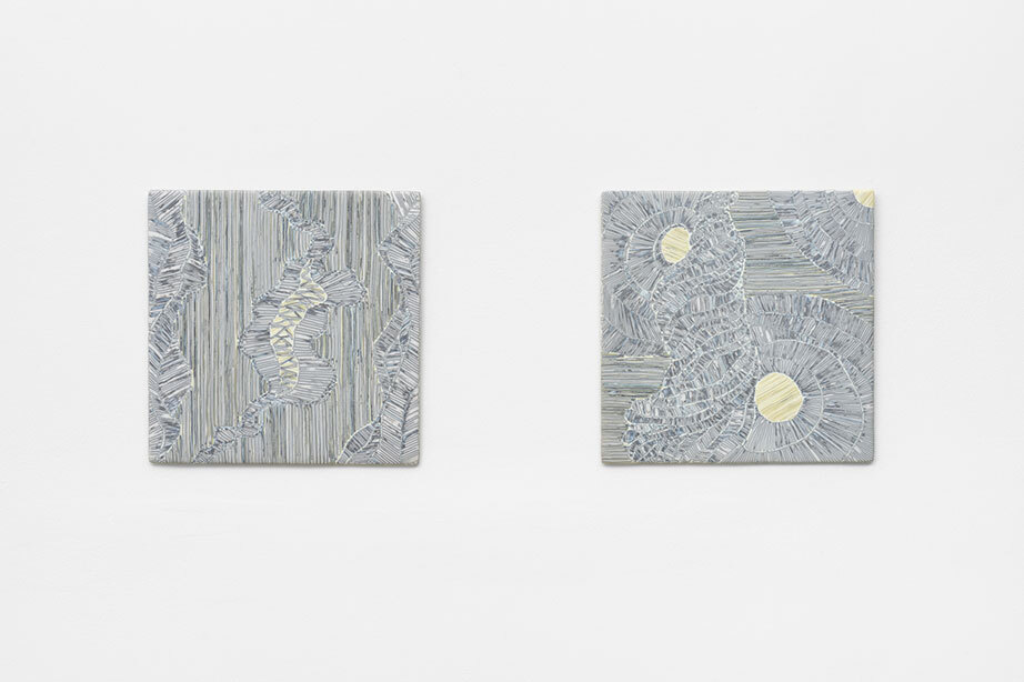 Two square artworks hang on a white wall. Their colors are white, black, and gold.