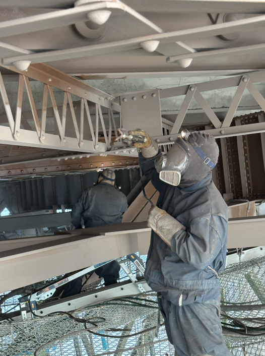 Workers wearing hazmat suits and respirators remove paint from the José Rizal. 