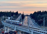 Transit train overlooking major highway with cars, trees, and sunset in background