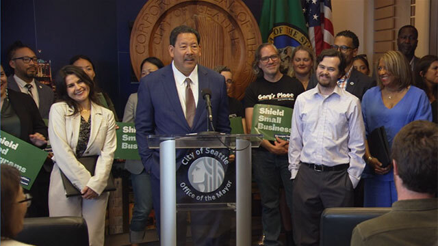 Mayor Bruce Harrell stands at podium, group stands to sides and behind