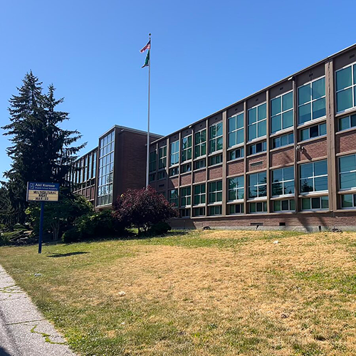A two-story building with windows along both floors with blue message board pictured on grass in front