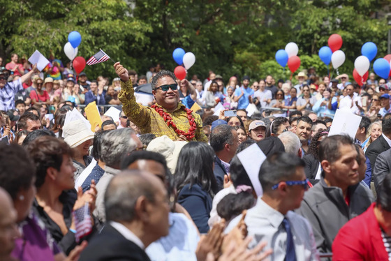 A person waving an American flag in crowd with red, white, and blue balloon in the background