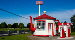A small white and red gas station that is shaped like a tea kettle