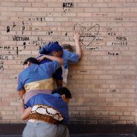 performance of four people leaning on each other against a brick wall