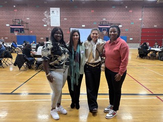 Four people, whose names are listed in the caption are standing arm and arm in the gym at Garfield High School