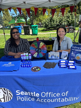 OPA staff sitting at a table with a blue tablecloth. OPA branded tote bags, brochures and other prizes are on the table.