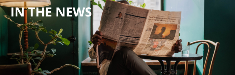 Header that says In the News in bold, white font. In the background is a person whose face is covered by an open newspaper 