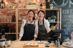 Two smiling business owners standing behind counter in coffee shop.