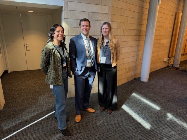 OPA team members posing for a photo against a light color tile block wall and dark patterned carpeting.