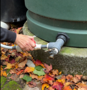 Close-up of a hand turning the valve on a green cistern with colorful fall leaves in foreground