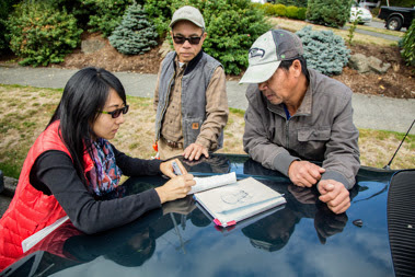 A group of three people review papers on the hood of a truck