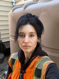 Head shot photo of white woman with dark hair wearing hi-vis orange vest