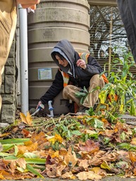 a woman in a hi-vis orange vest stoops in front of a cistern to point to valve