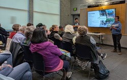 Group of people listen to a woman presenting a slide show