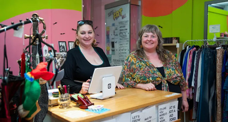 Two women standing behind a counter with a register with clothing around them