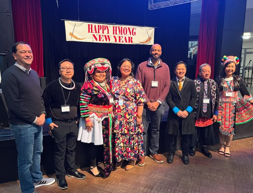 a group of people standing in front of a sign that reads Hmong New Year