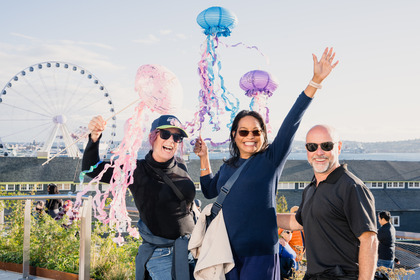 two women and a man holding paper jellyfish in front of the ferris wheel and puget sound