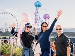two women and a man wholding paper jellyfish on the waterfront