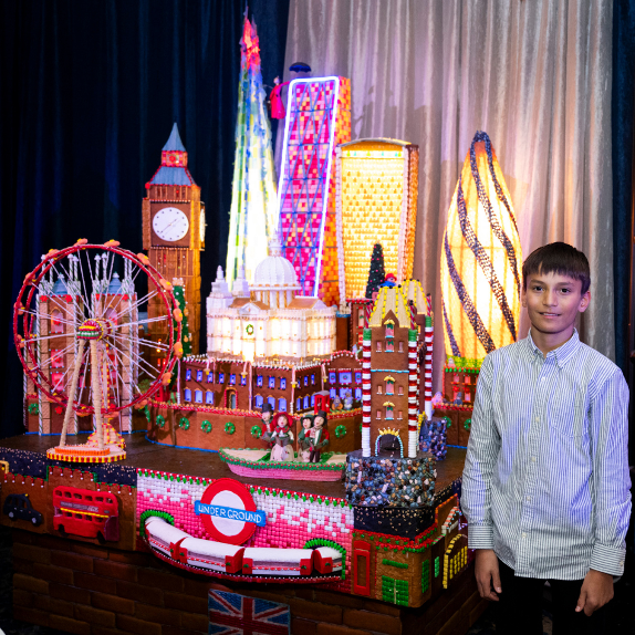 boy standing next to gingerbread village
