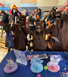 Three kids dressed up as cockroaches for Harvest Fest. They are wearing black sunglasses and waving their hands in the air