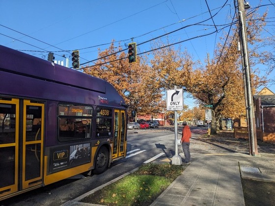 A person waits at a crosswalk as a Route 7 bus travels along Rainier Ave S in a red bus lane, funded in part by STM. Photo: SDOT.