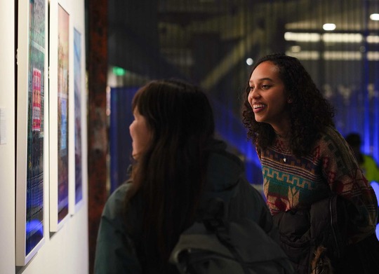 Two women look at art on gallery wall with smiles