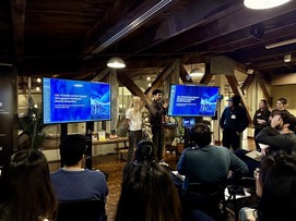 Two people presenting to the hackathon crowd as they show a powerpoint presentation