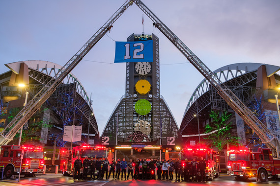 Seattle firefighters stand in front of several fire apparatus flying a 12s flag in support of the Seahawks