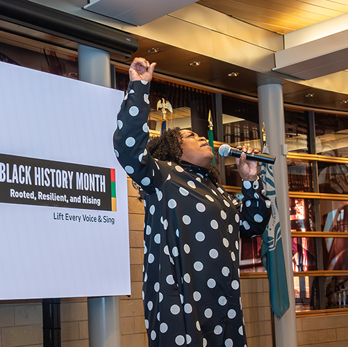A Black woman passionately singing into a microphone with one hand raised in the air.