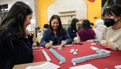 Three Asian American youth sitting at a table playing a game with tiles