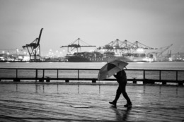 A person walks on a wet sidewalk, holding an umbrella to shield themselves from the rain.