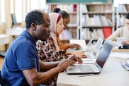 A group of diverse individuals seated at a table, each using a laptop for collaborative work or discussion.