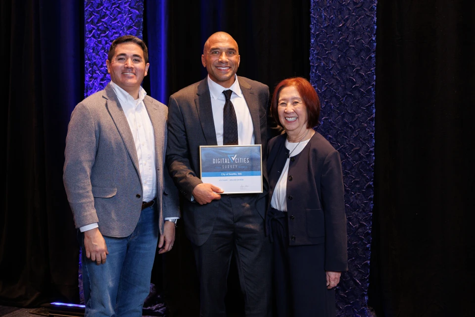 Two men and a woman proudly hold an award against a black backdrop, celebrating their achievement together.
