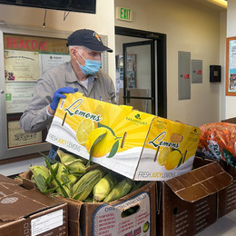 An older man wearing a mask over his mouth and gloves unloaded boxes of donated food