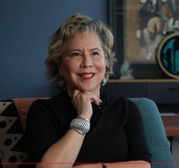 A Latina/Native American woman with short blond/grey hair sitting in an office smiling