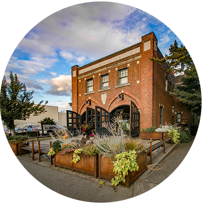 Exterior of a brick building with two large sets of bay doors open in front and a landscaped patio