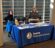 Color photo of two women in front of SMA table at Records and Information Management Month event