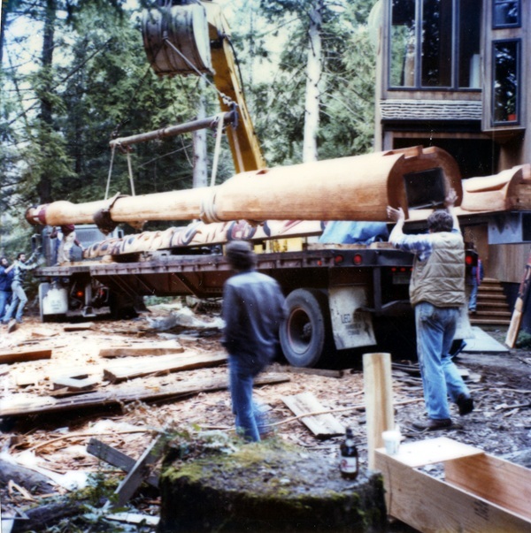 Color photo of newly-carved totem poles being loaded onto flatbed truck