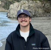 Nick Anspach has dark hair, a mustache and wears glasses