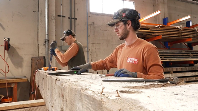 Two men remove nails from a wood beam.