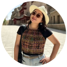 A Chinese woman wearing sunglasses and a straw hat smiling with Chinese architecture in the background