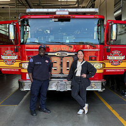 A Black firefighter and a Vietnamese woman pose in front of a Seattle Fire Department fire truck