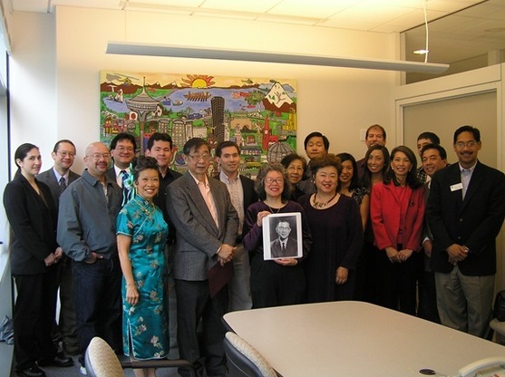 Color photo of a group of people standing around a photo of former Councilmember Wing Luke.