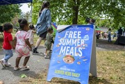 People in public walking past sign that reads Free Summer Meals Served Here Daily