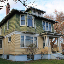A large three story house with green siding on the top floor and yellow siding on the ground floor