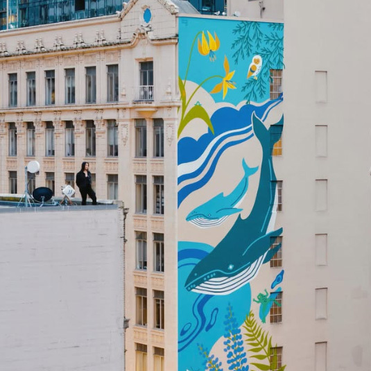 A mural on the side of building featuring humpback whales, ocean waves, plants, and other animals. Mural by Stevie Shao